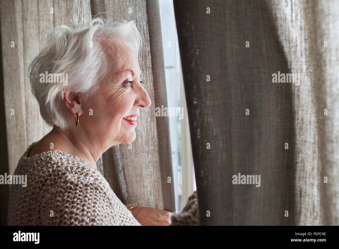 Senior donna guardando fuori della finestra Foto Stock