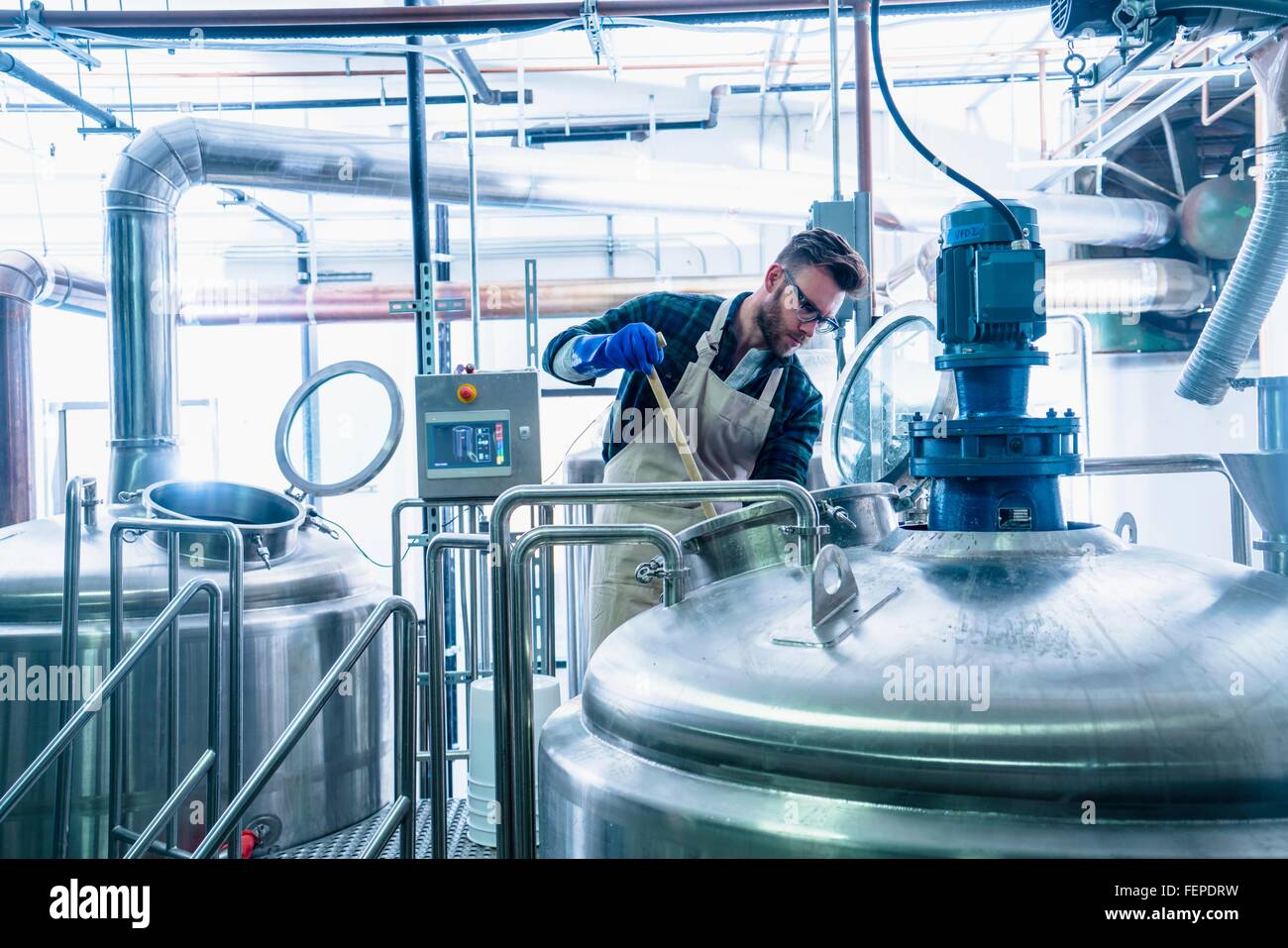 Giovane uomo in birreria indossando grembiuli e guanti protettivi di birra di test nel serbatoio Foto Stock