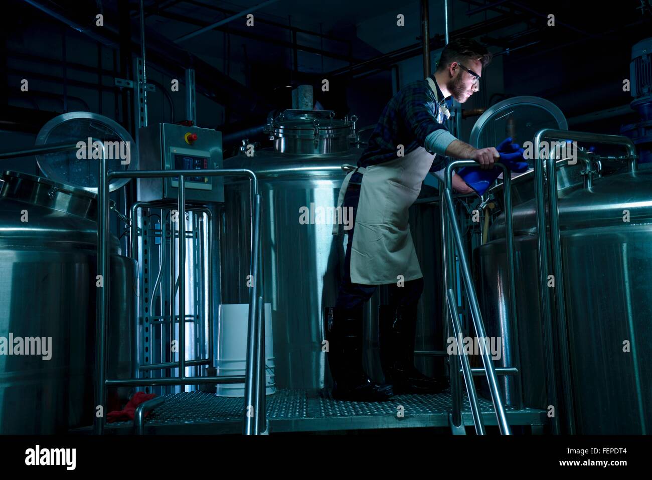 Vista laterale del giovane uomo nella fabbrica di birra guardando nel serbatoio di fermentazione Foto Stock