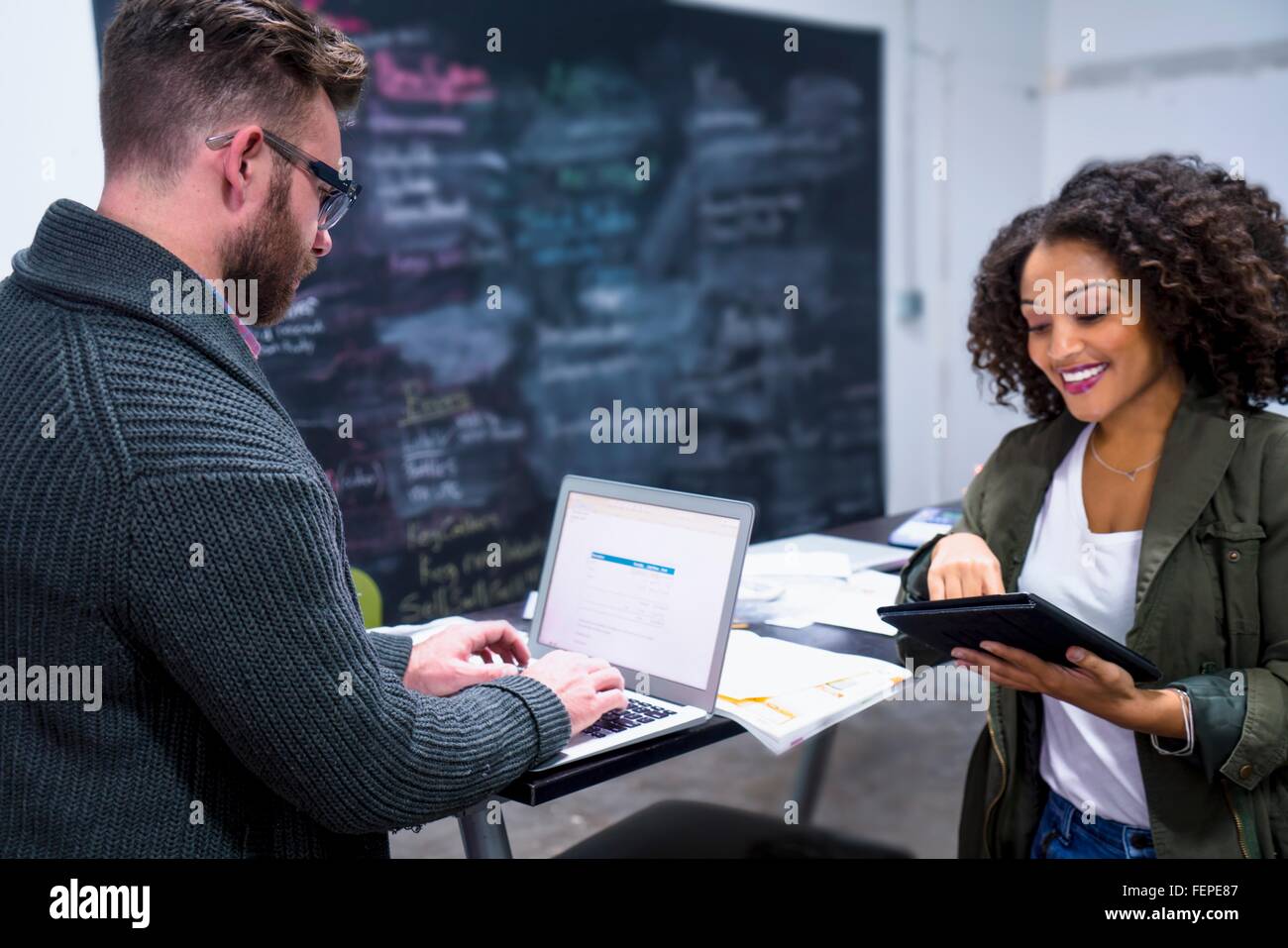 I colleghi nel posto di lavoro utilizzando tavoletta digitale portatile e sorridente Foto Stock