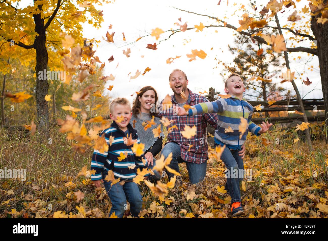 Vista frontale della famiglia dando dei calci a foglie di autunno guardando sorridente della fotocamera Foto Stock
