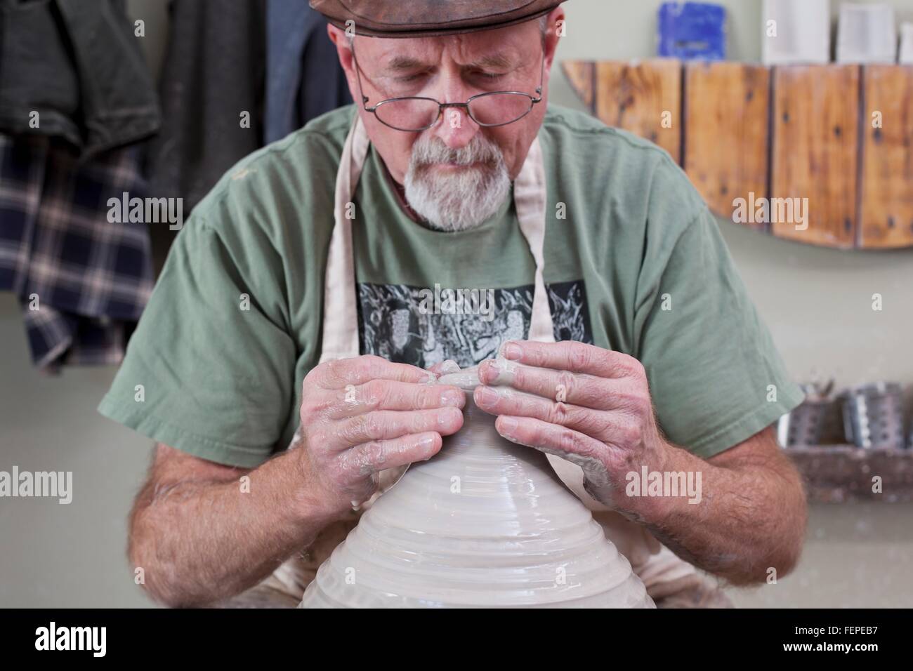 Potter indossando il tappo piatto sagomatura di finitura vaso di creta, guardando verso il basso Foto Stock