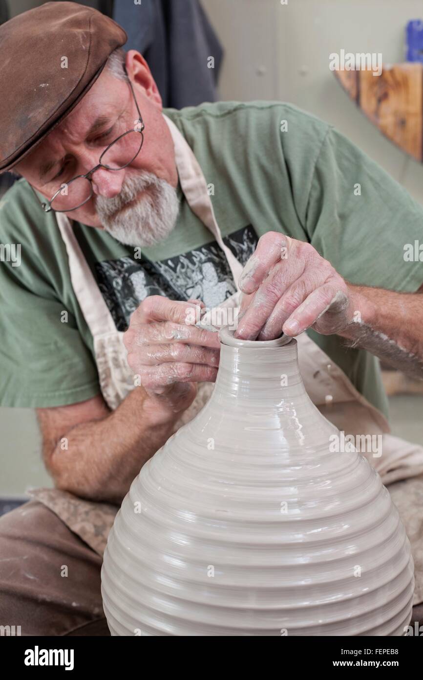 Potter indossando il tappo piatto sagomatura di finitura vaso di creta, guardando verso il basso Foto Stock