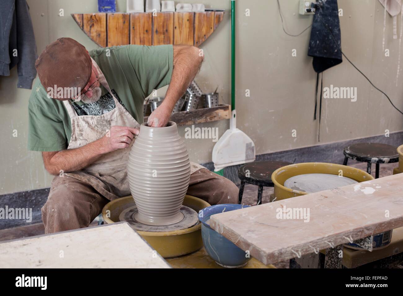 Potter indossando il tappo piatto seduti al volante di ceramiche di sagomatura vaso di creta Foto Stock
