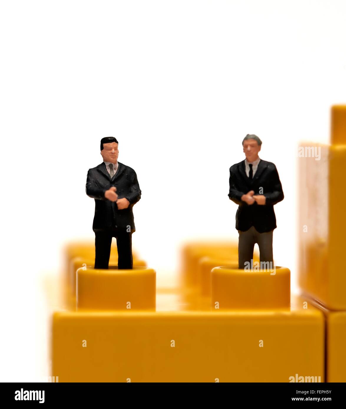 Miniatura di figurine di uomini di affari in giacca permanente sulla plastica gialla mattoni da costruzione Foto Stock