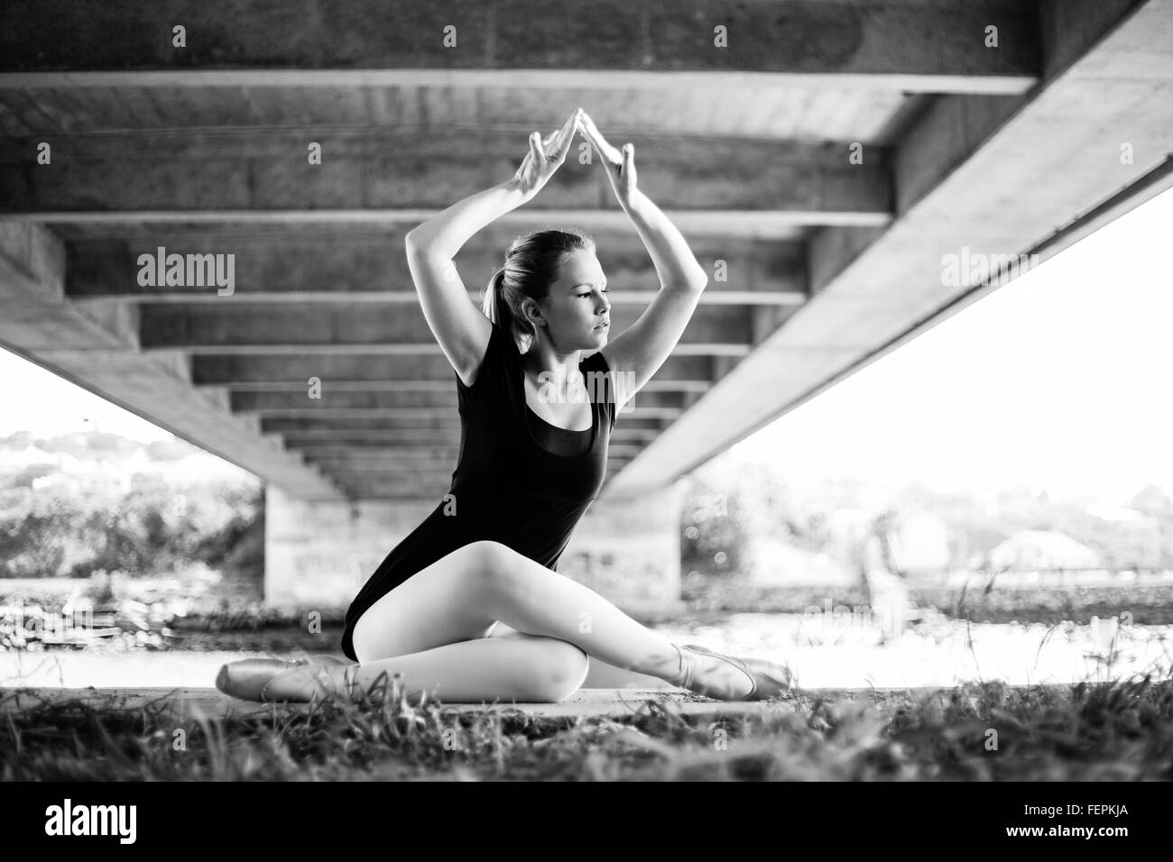 Una bellissima giovane ballerina è in posa sotto un ponte con il fiume dietro di lei un sacco di belle linee principali per belle arti Foto Stock