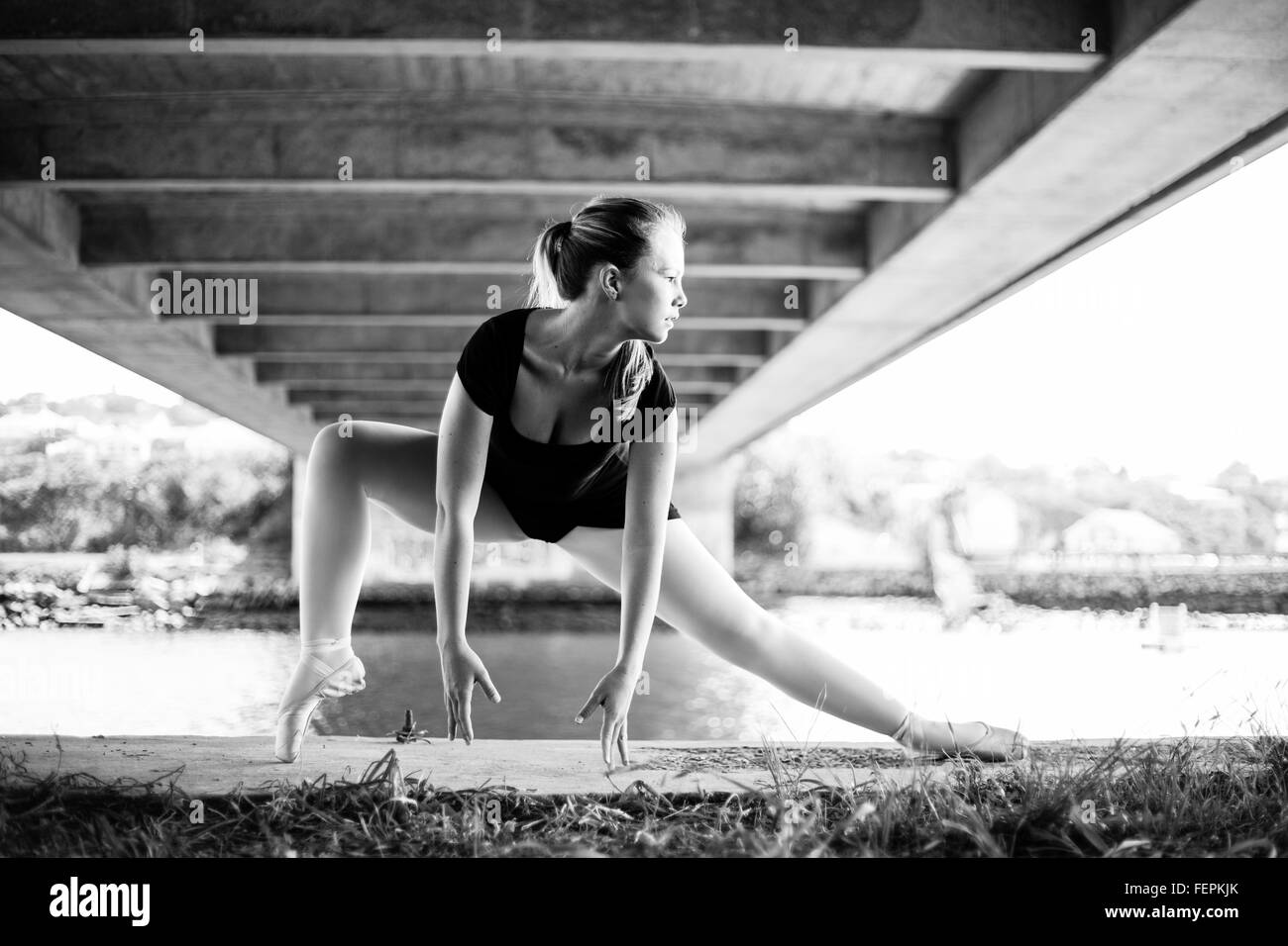 Una bellissima giovane ballerina è in posa sotto un ponte con il fiume dietro di lei un sacco di belle linee principali per belle arti Foto Stock