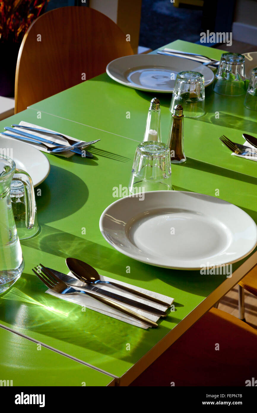 Cafe tabella stabilite per un pasto con i coltelli forchette e cucchiai porcellana bianca Piatti bicchieri e sale e pepe Set condimento Foto Stock