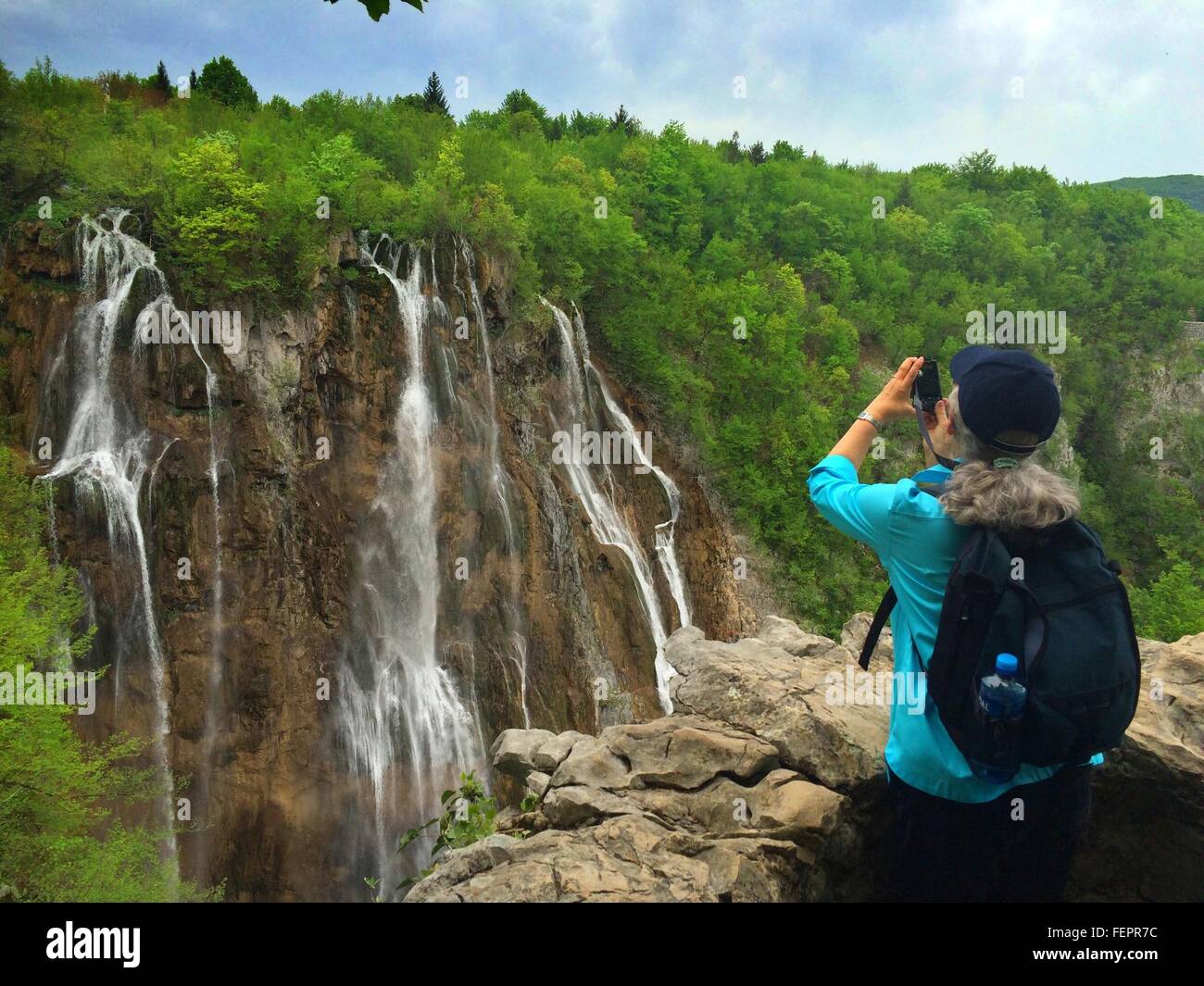 Vista posteriore della donna a fotografare una cascata presso il Parco Nazionale dei Laghi di Plitvice Foto Stock