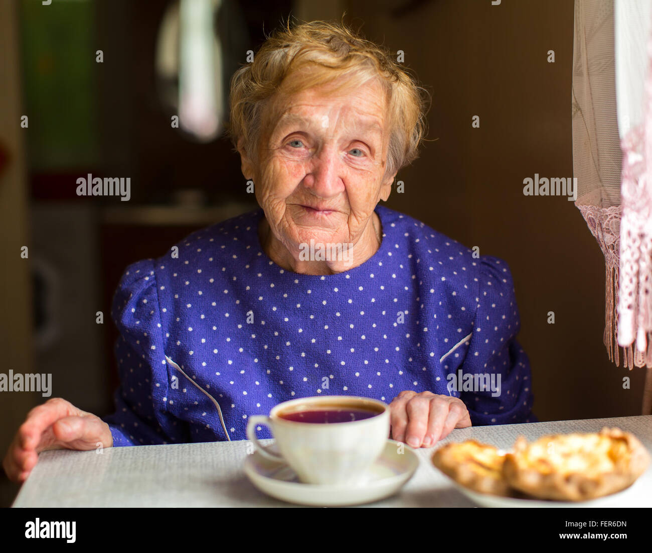 Una donna anziana seduta al tavolo e bere il tè. Foto Stock