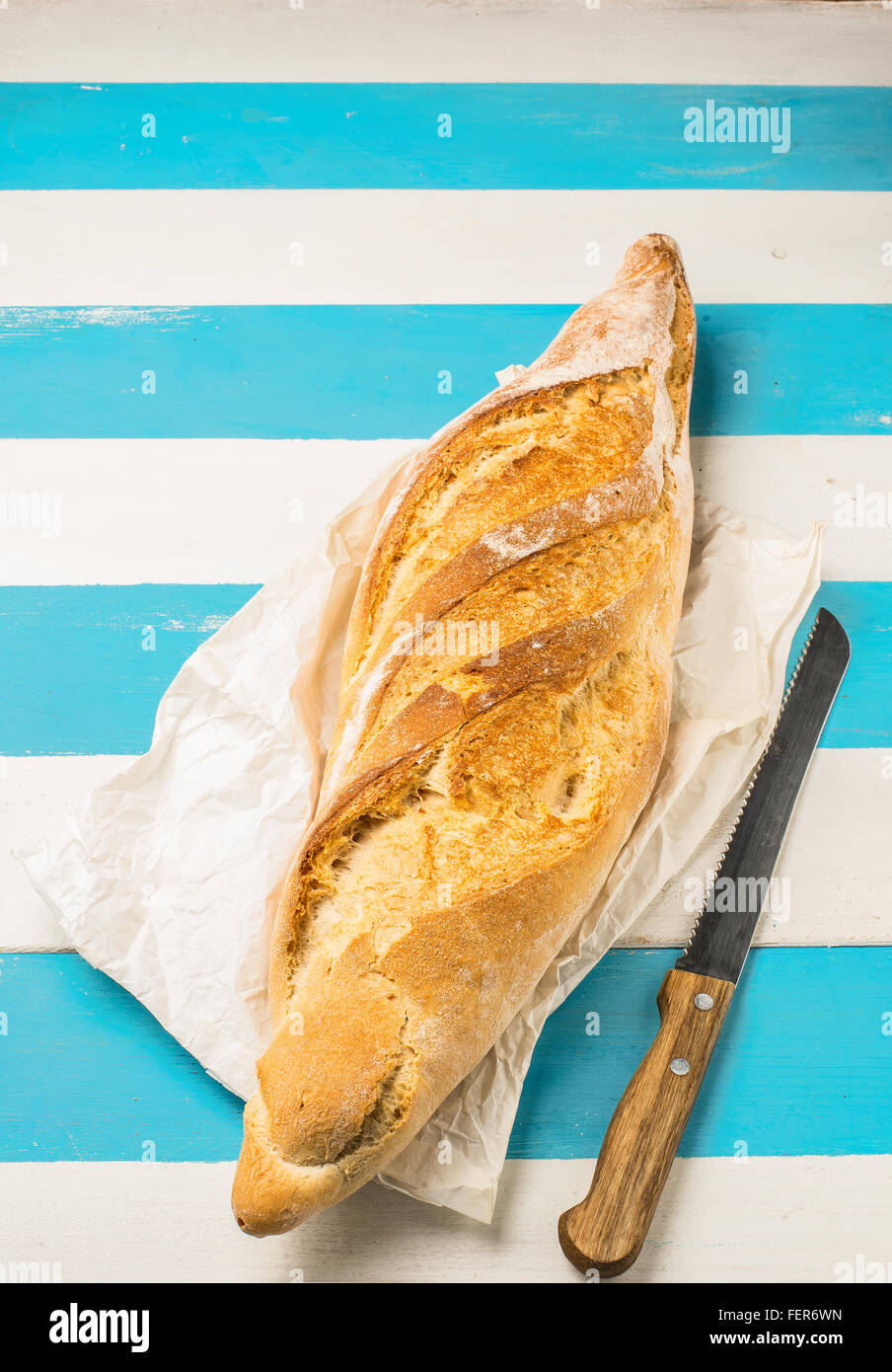 Filone di pane in un negozio di generi alimentari sacchetto di carta (stile europeo) su un rustico Mediterraneo bianco e blu tavolo in legno. Foto Stock