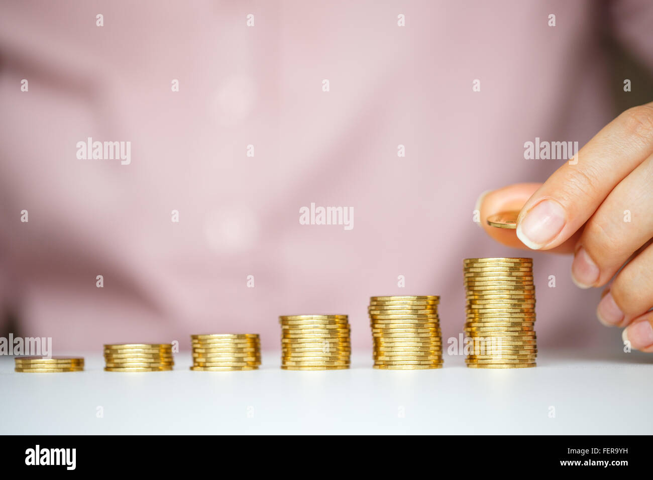 Risparmio di mano femminile di impilamento delle monete in oro in colonne crescente Foto Stock