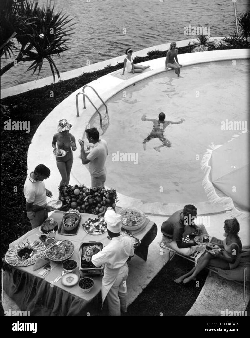 Una vivace festa in piscina con persone che si godono una giornata di sole con nuoto, socializzazione e attività ricreative. L'immagine riflette un'atmosfera rilassata tipica degli incontri estivi. Foto Stock