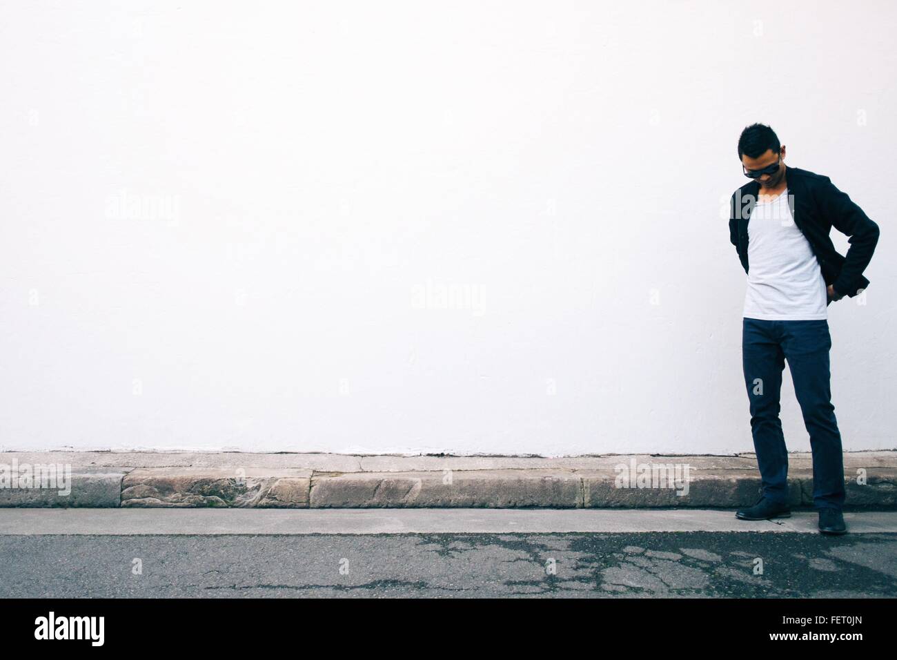 Giovane uomo guardando giù in piedi contro il muro bianco Foto Stock