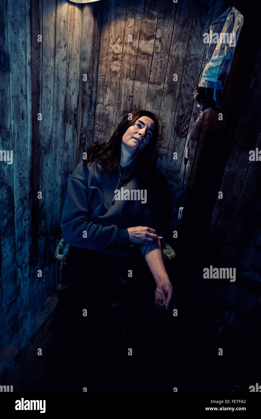 Lone donna junkie in un capannone di legno con una flebo IV nel suo braccio Foto Stock