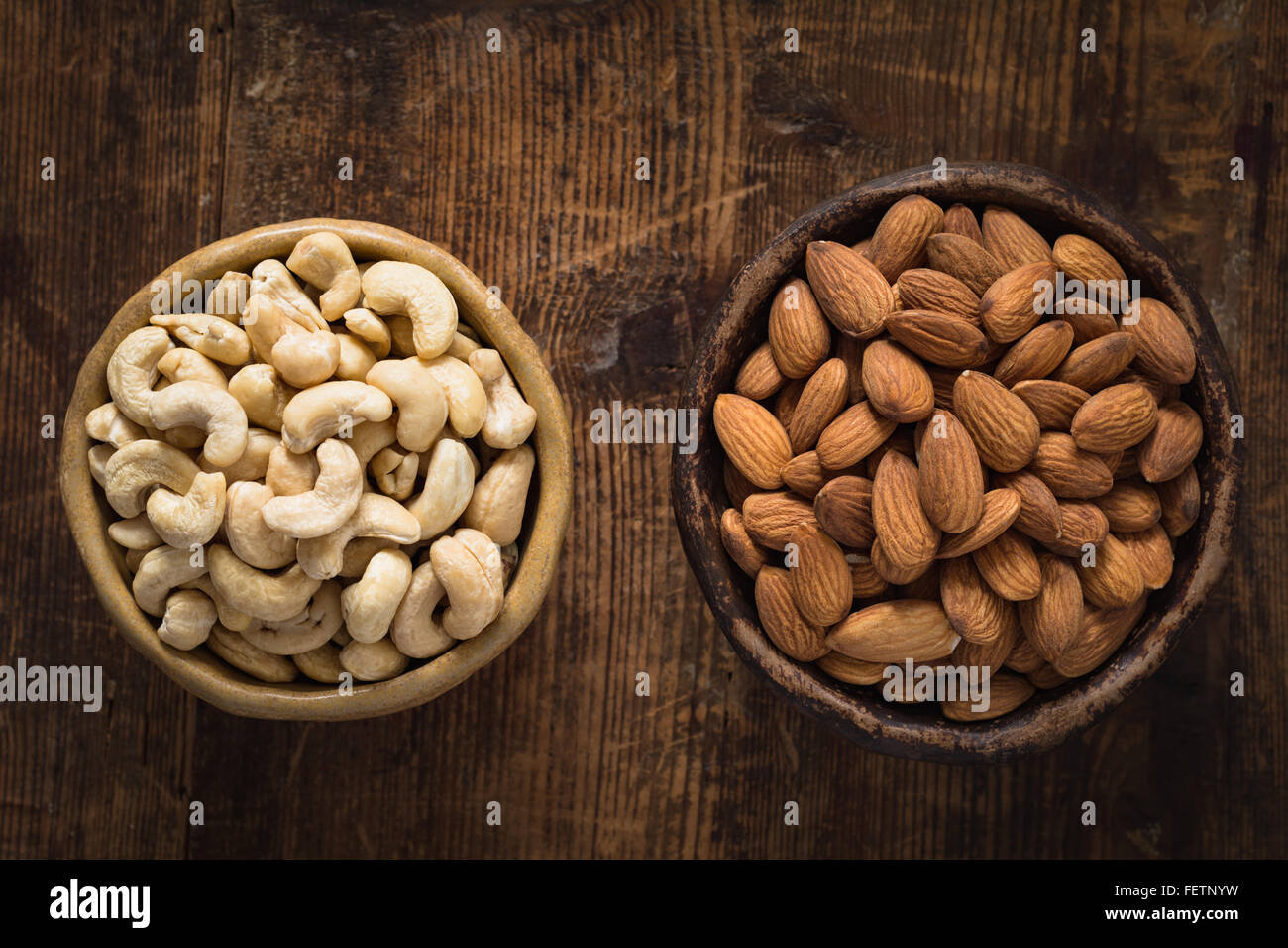 Mandorle e anacardi nella ciotola sulla texture di sfondo di legno. Tabella vista superiore del cibo. Luce naturale Foto Stock