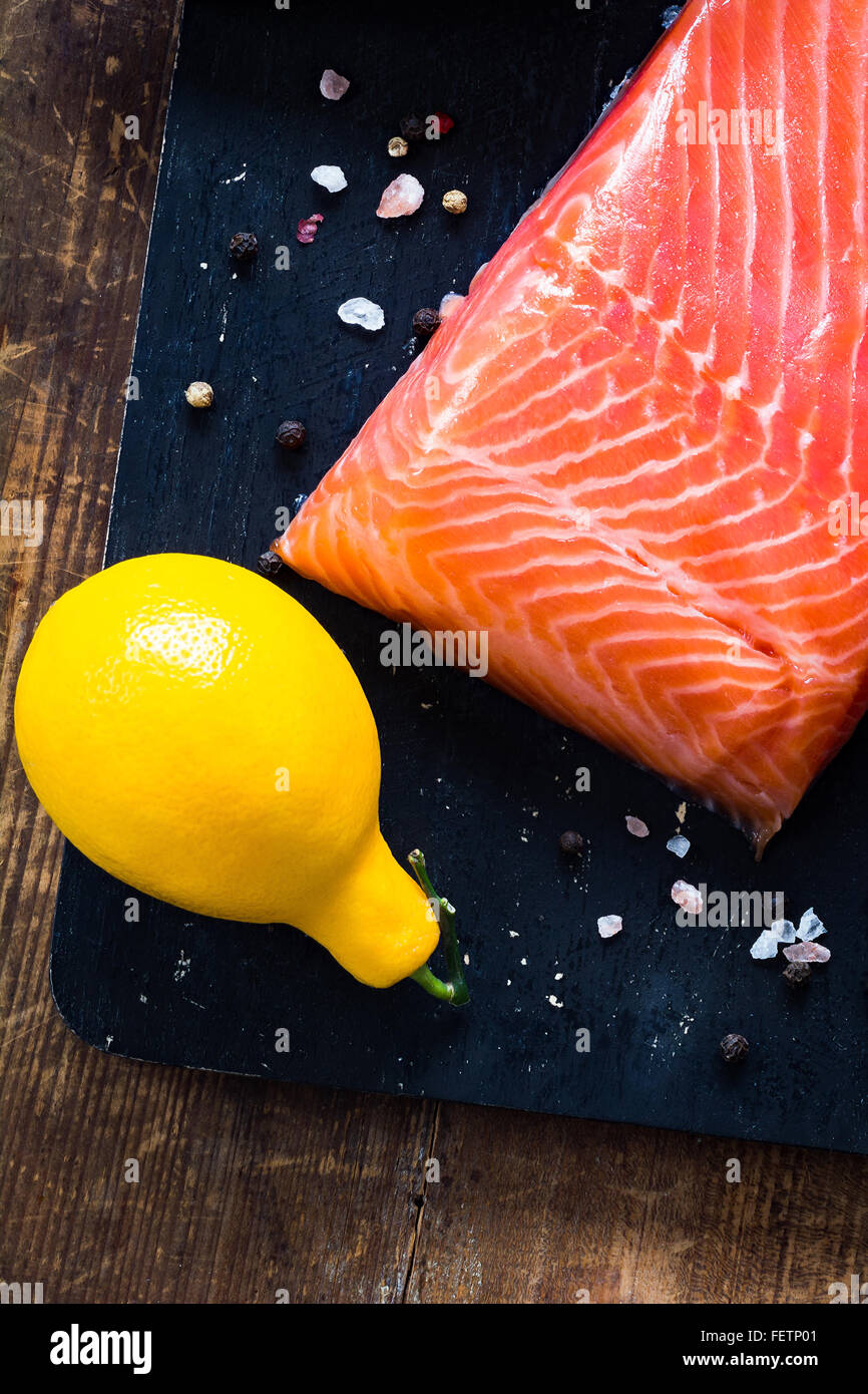 Filetto di salmone, limone, rosa di sale e di pepe sul tagliere di legno. Vista superiore Foto Stock