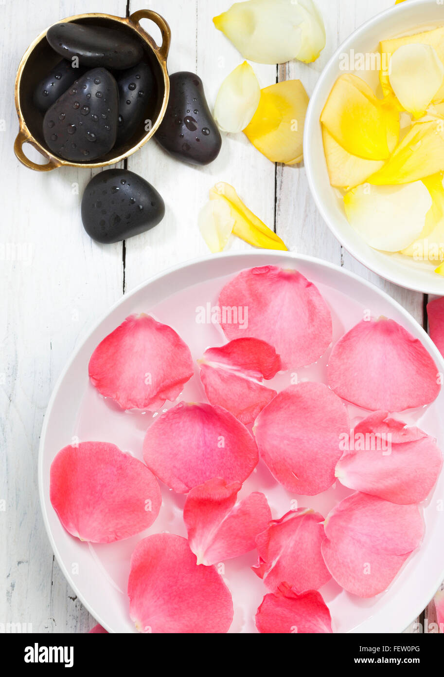 Concetto di spa - rosa e giallo petali di rosa in ciotole di acqua, massaggi pietre nel recipiente di ottone, vista dall'alto Foto Stock