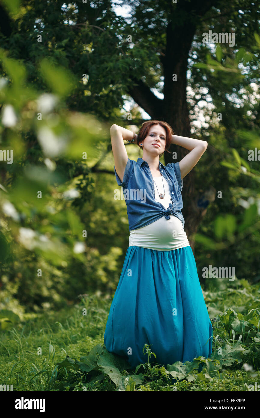 Bella giovane donna incinta per godersi la natura e il sole in estate Park. A piena altezza verticale, cercando nella fotocamera. Foto Stock