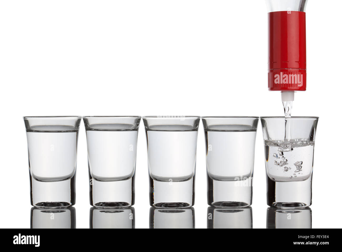 La vodka versando in bicchierini in piedi in fila, isolato su uno sfondo bianco, percorso di clipping incluso. Foto Stock