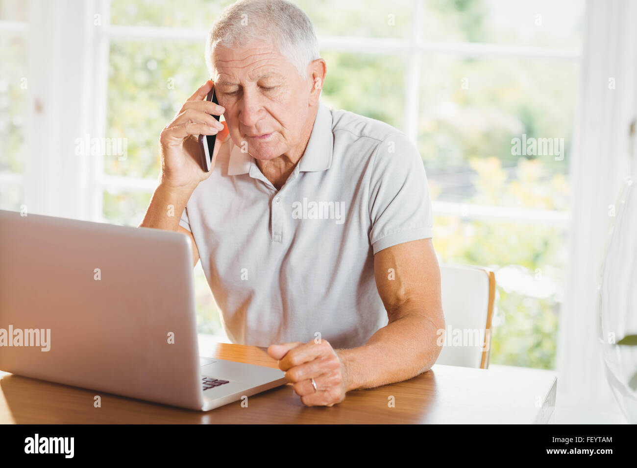 Senior concentrato un uomo guarda il portatile e telefono chiamando Foto Stock
