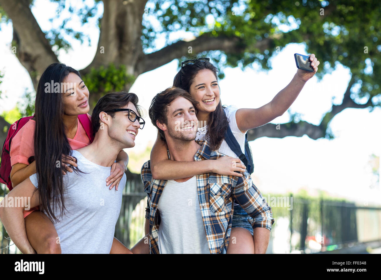 Hip uomini dando piggy back per le loro fidanzate e tenendo selfie Foto Stock