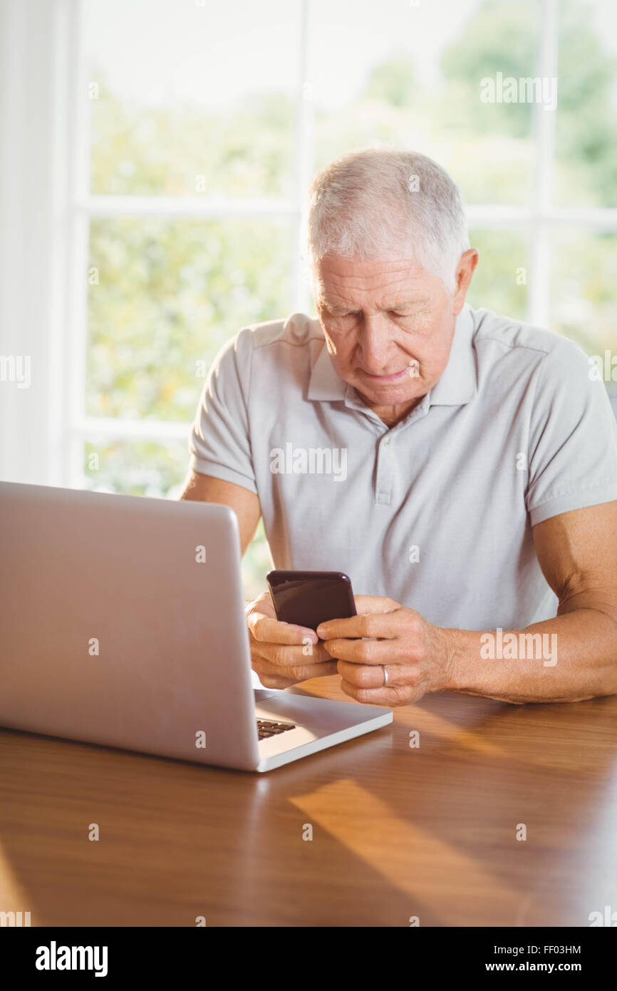 Focalizzato uomo anziano utilizza lo smartphone e il computer portatile Foto Stock