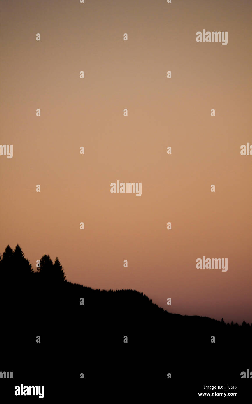 Un cielo chiaro al tramonto con tenui rosa, arancione e marrone Colori e stagliano colline e alberi. Foto Stock