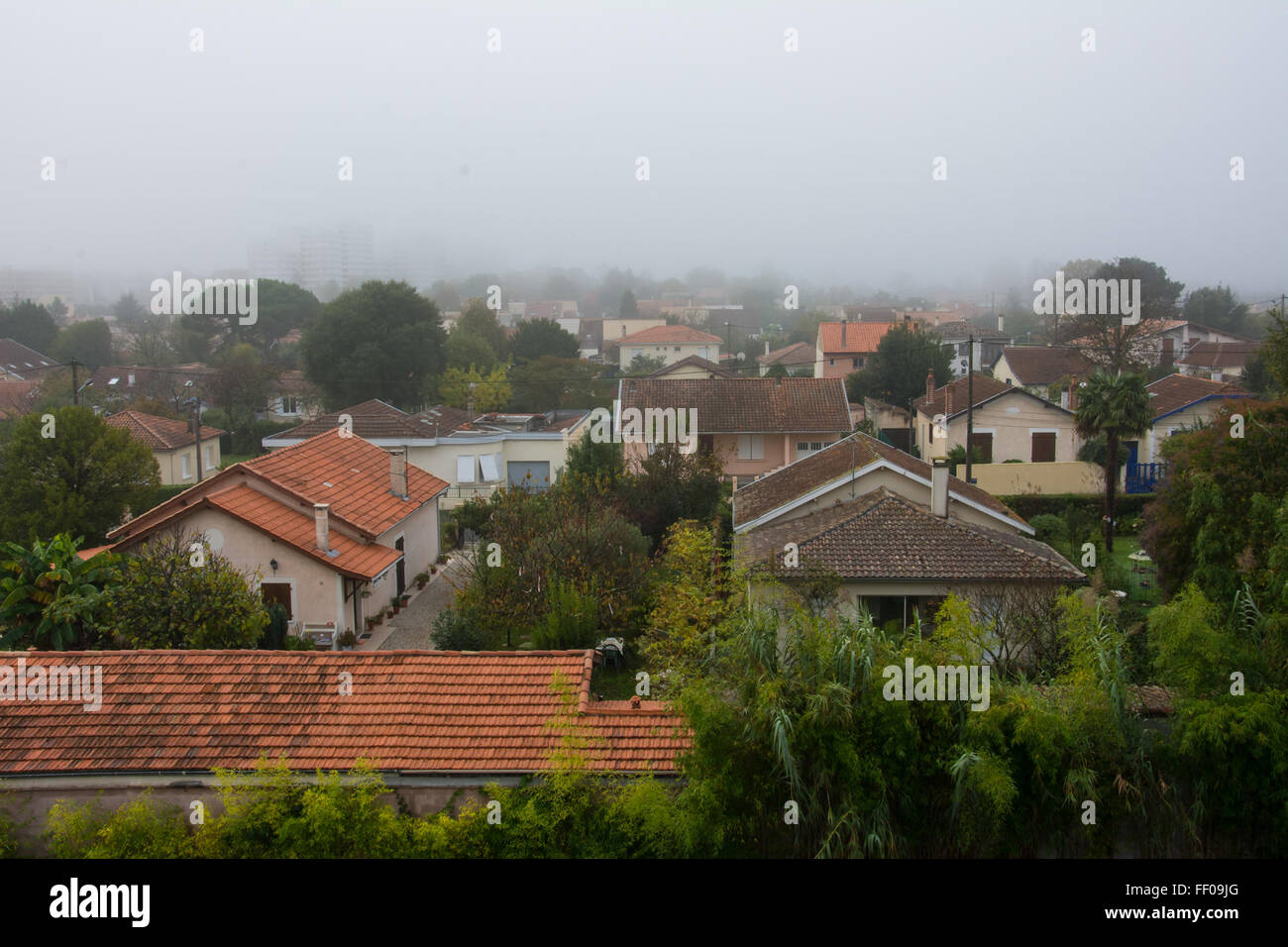 Una vista sui tetti residenziali, parzialmente oscurati dalla nebbia e dalla foschia, con l'orizzonte che si allunga in lontananza. La scena cattura un ambiente urbano influenzato da fattori ambientali, come lo smog e l'inquinamento. Foto Stock