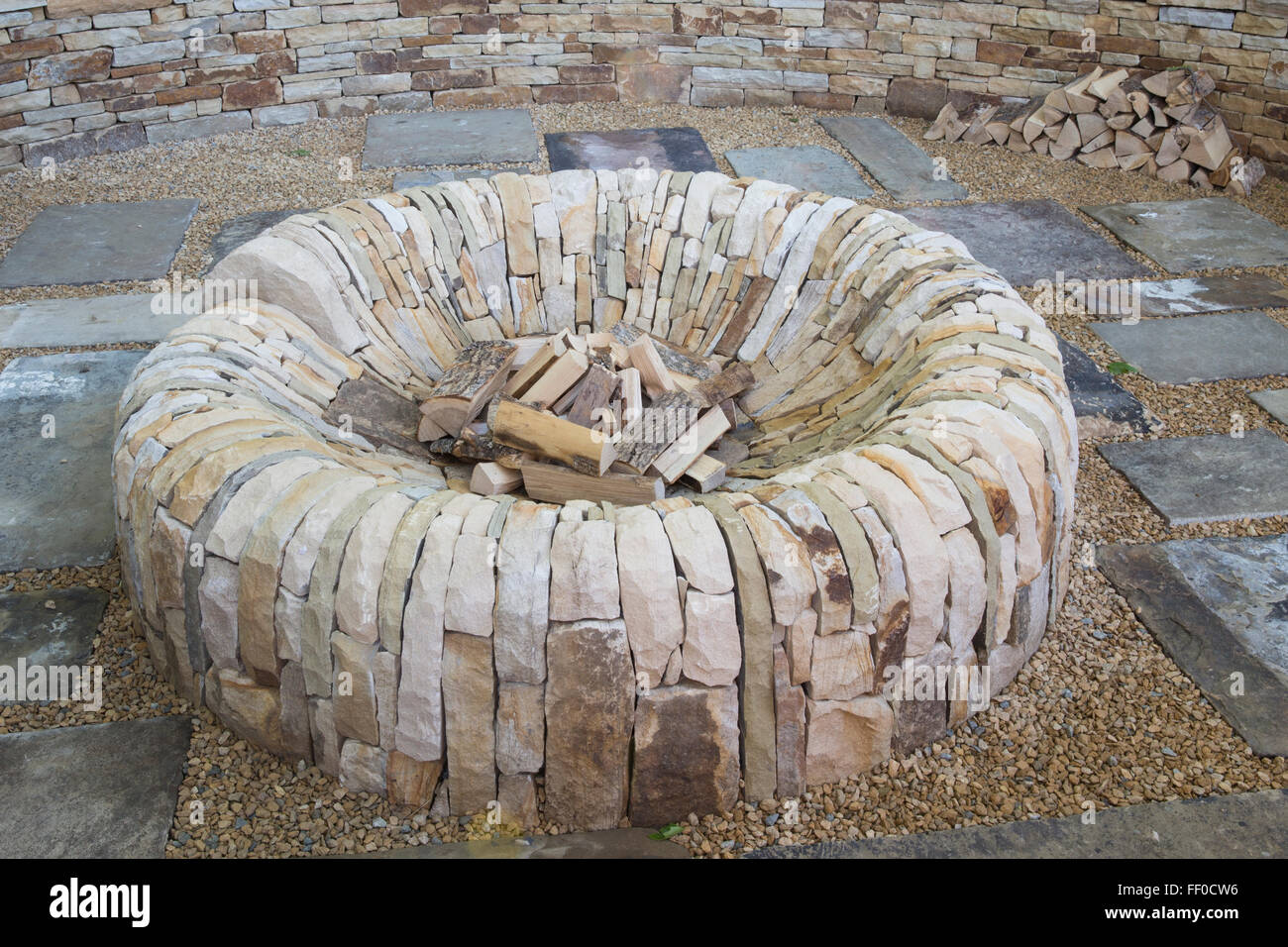Giardino con una buca circolare di fuoco fatta di pietra in una ghiaia e pietra pavimentata area patio UK Foto Stock