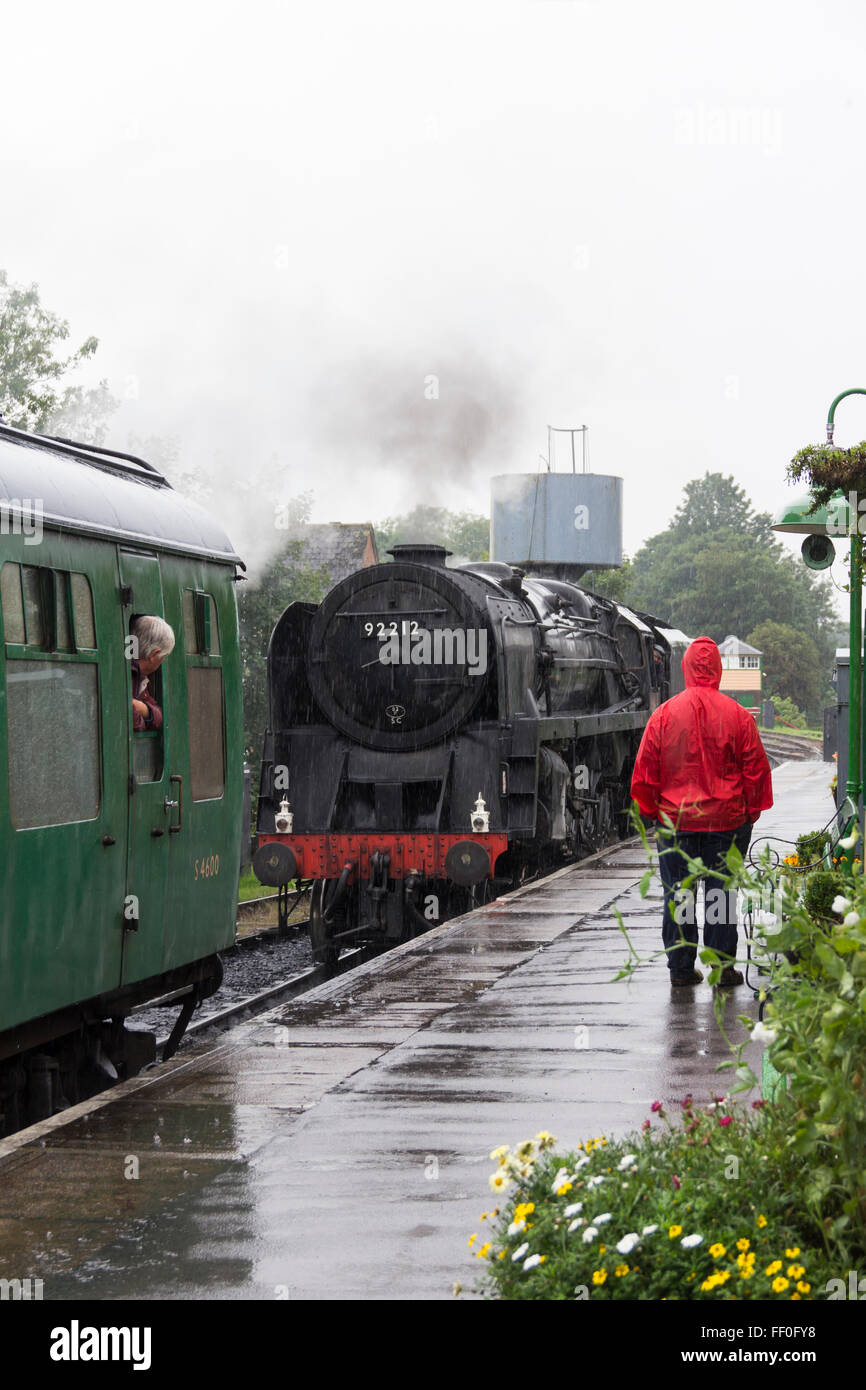 Un appassionato di appassionati di treni si erge in heavy rain guardando la classe 9F motore a vapore 92212 spostare verso il suo treno alla stazione di Alton. Foto Stock
