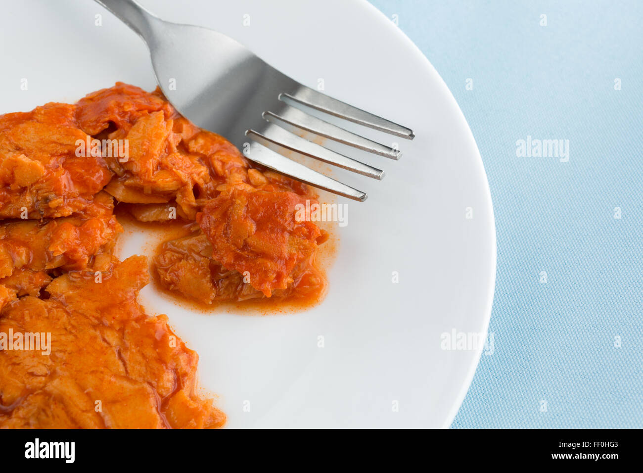 Una piccola porzione di piccante aromatizzata rosa salmone su una piastra con la forcella sulla cima di un tovagliolo blu illuminato con luce naturale. Foto Stock