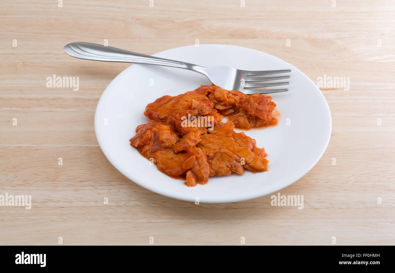 Vista laterale di una piccola porzione di piccante aromatizzata rosa salmone su una piastra con la forcella sulla cima di un legno tavolo illuminato con l naturale Foto Stock