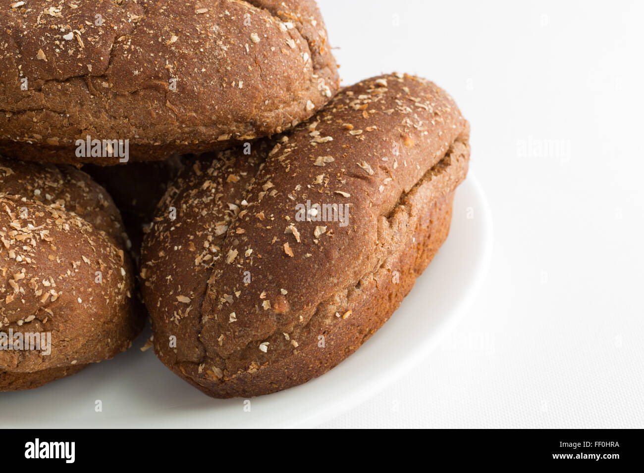 Chiudere la vista di un gruppo di pane appena sfornato multi-rotoli di granella su una piastra bianca sulla cima di una tovaglia bianca Foto Stock