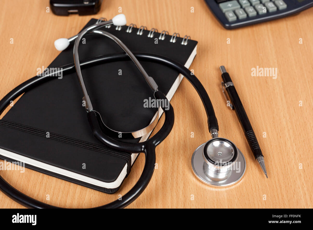 I medici lo stetoscopio posa su un blocco note su una scrivania con una penna e una calcolatrice Foto Stock