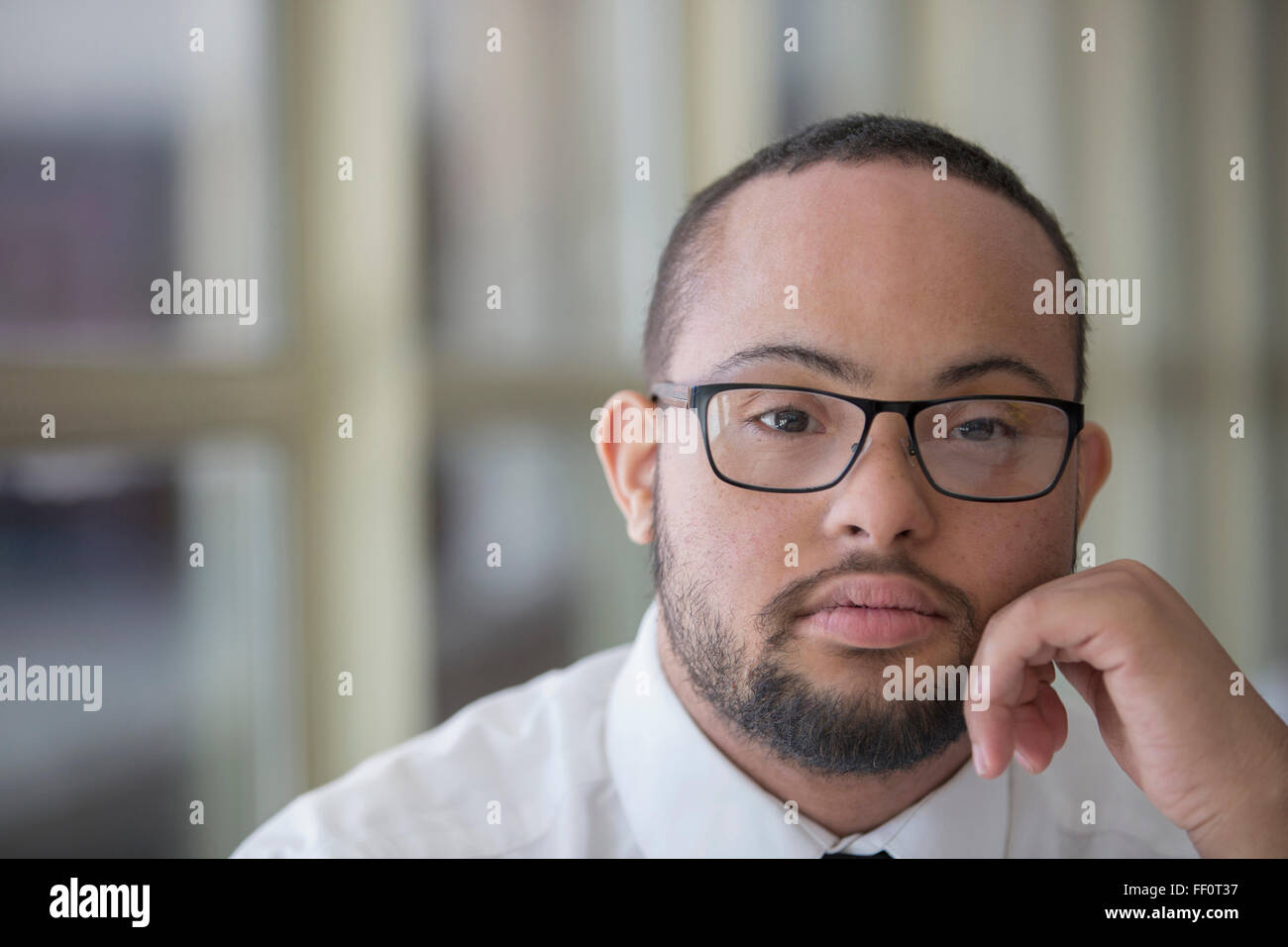 Razza mista uomo con la sindrome di down in appoggio mento in mani Foto Stock