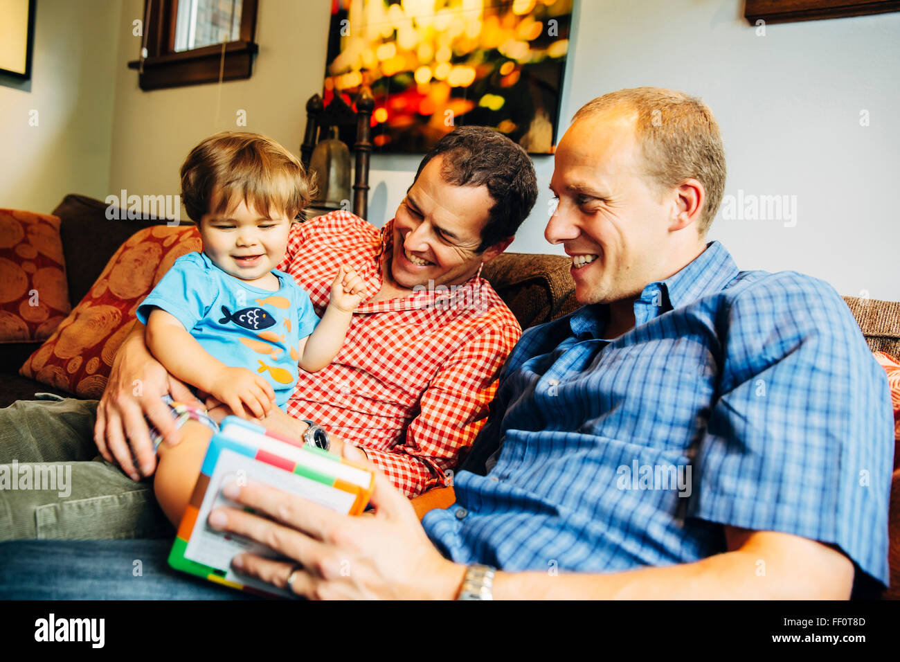 Gay padri giocando con il bambino figlio sul divano Foto Stock
