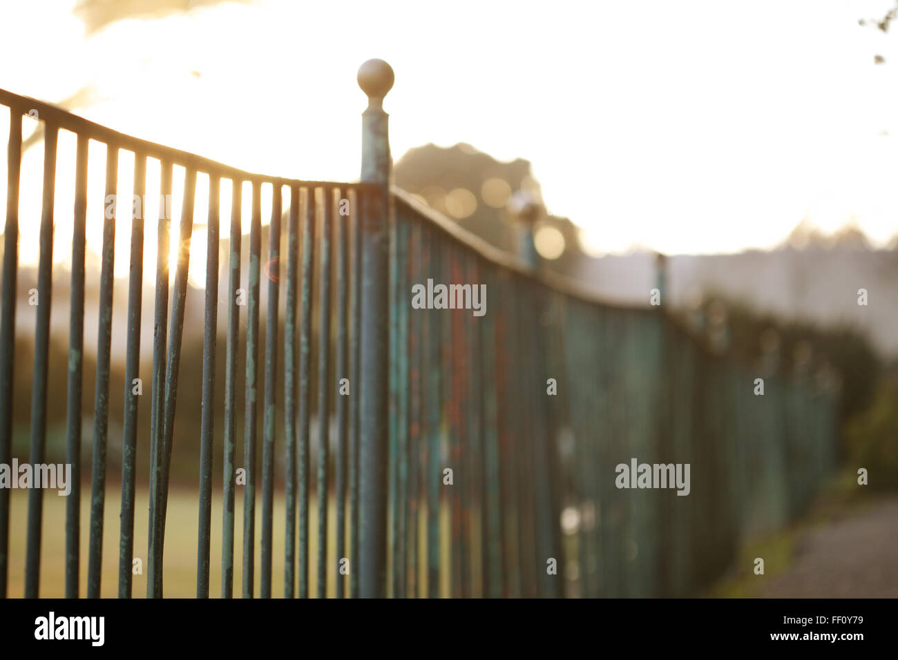 Un close-up di un recinto con un po' di sole in background che brilla attraverso le barre metalliche della recinzione. Foto Stock