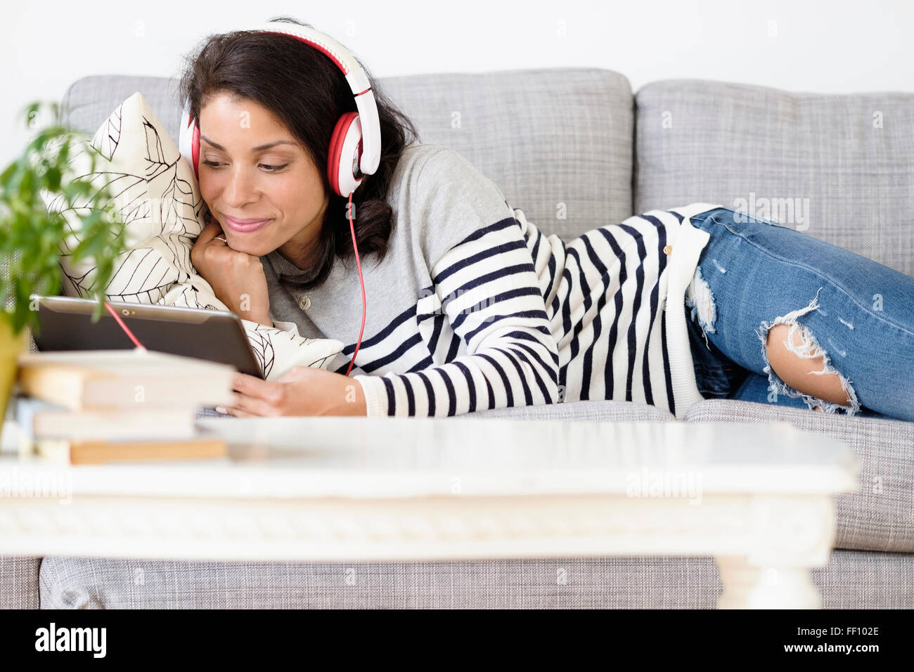 Razza mista donna in ascolto delle cuffie sul divano Foto Stock