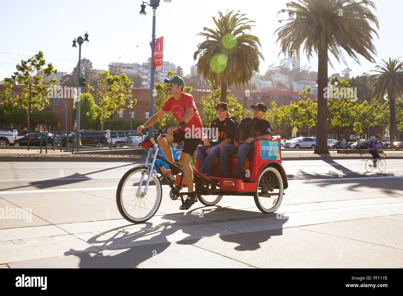 Un maschio Bike Taxi Driver il trasporto di due passeggeri maschi, tutti su una soleggiata giornata calda lungo San Francisco Embarcadero. Foto Stock