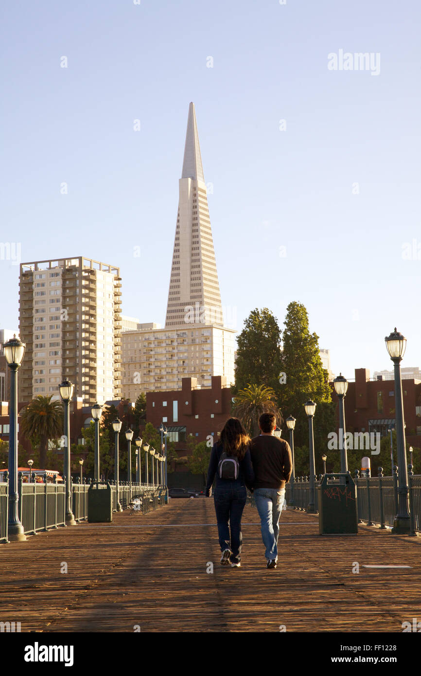 Un giovane a piedi lungo una passerella sull'Embarcadero a San Francisco con la Piramide Transamerica in background. Foto Stock