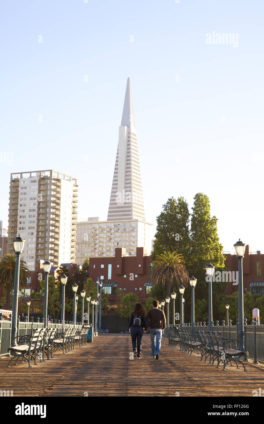 Un giovane a piedi lungo una passerella sull'Embarcadero a San Francisco con la Piramide Transamerica in background. Foto Stock