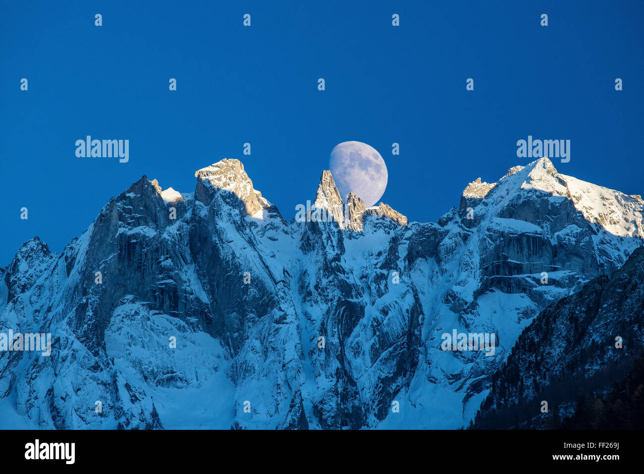 La luna appare dietro le montagne nevose illuminare i picchi al tramonto, Val Bondasca, alpi svizzere, Svizzera, Europa Foto Stock