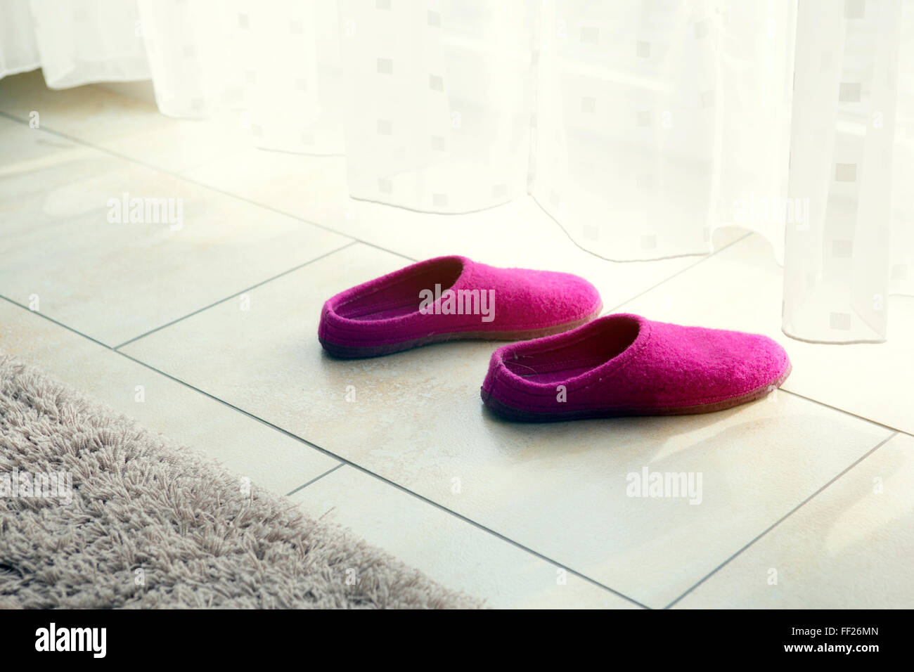 Pantofole viola sul pavimento da una tenda bianca Foto Stock