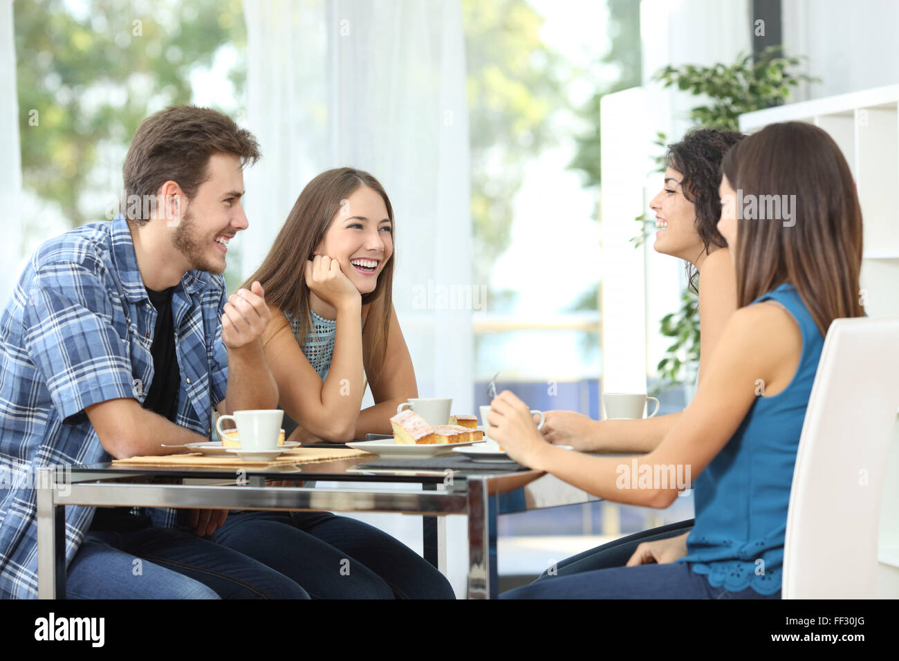 Un gruppo di 4 amici felici incontrare e parlare e mangiare dolci su un tavolo a casa Foto Stock