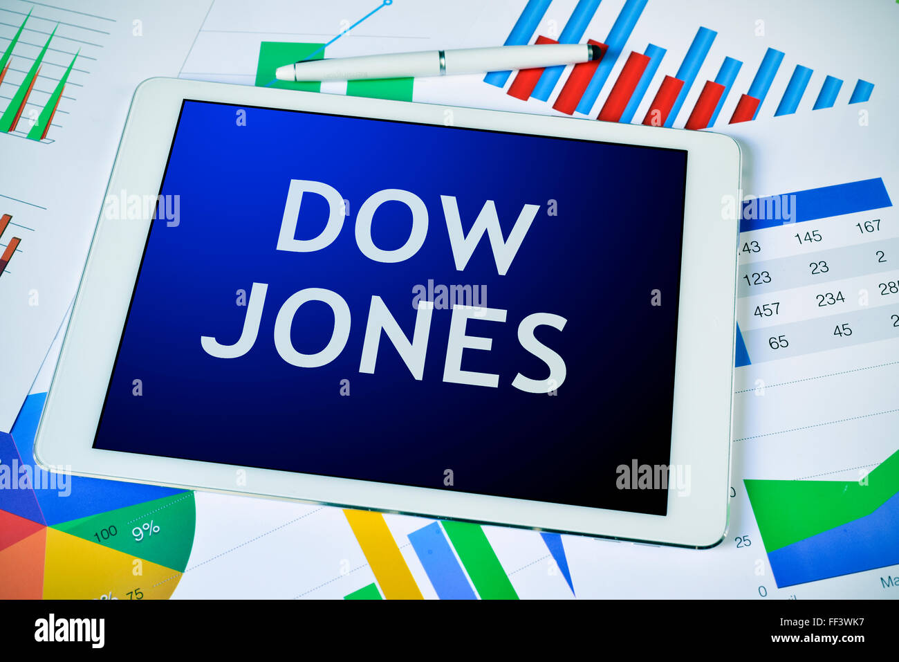 Un computer tablet con il testo Dow Jones, per il Dow Jones Industrial Average, su una scrivania piena di grafici Foto Stock