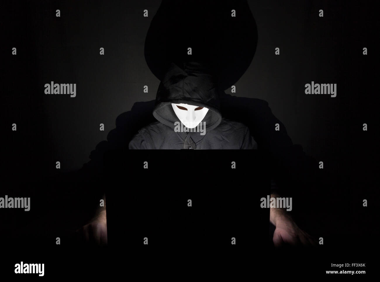 Un uomo mascherato in un laptop che simboleggia i pericoli di Internet Foto Stock