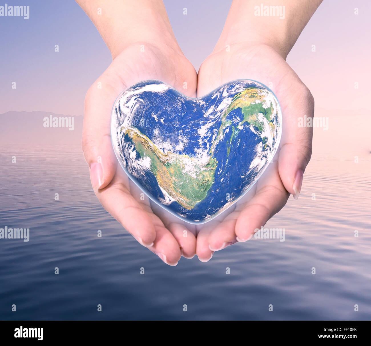 Mondo in forma di cuore con sopra le donne le mani umane su sfocato sfondo naturale blu turchese ciano tree e sky: World Heart hea Foto Stock