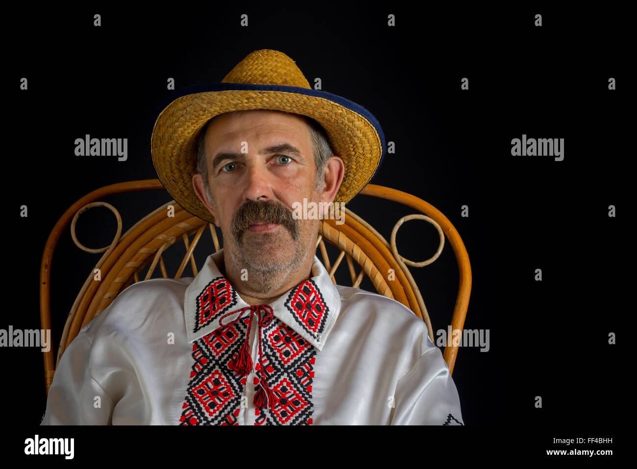 Ritratto del paese ucraino-uomo seduto in una sedia di vimini, indossando la paglia e abiti tradizionali (Vyshyvanka) Foto Stock