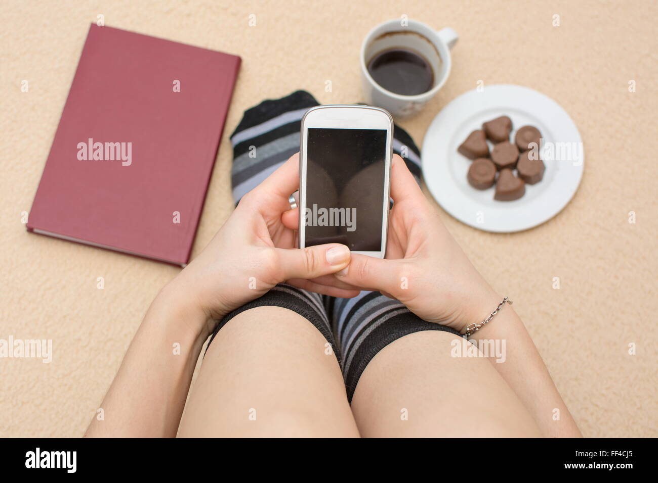 Ragazza utilizzando il suo telefono in letto circondato da libro caffè e dessert Foto Stock